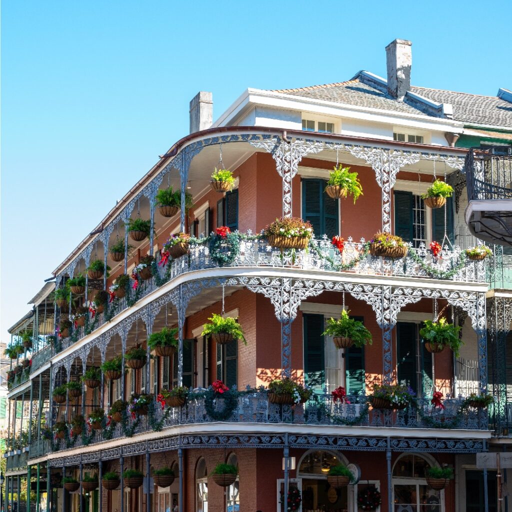 Corner of large beautiful building that has white balconies decorated with hanging plants and flowers